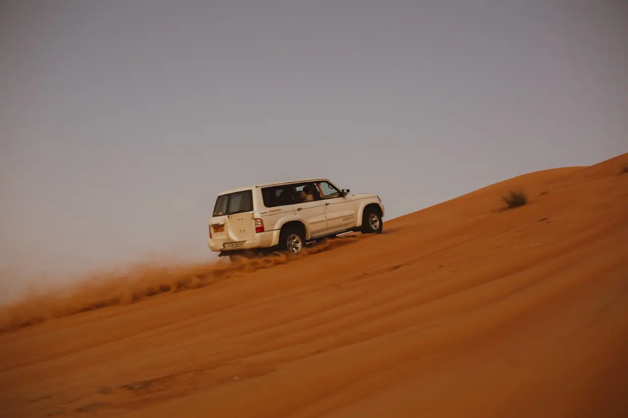 A white 4×4 driving up the side of an orange sand dune.