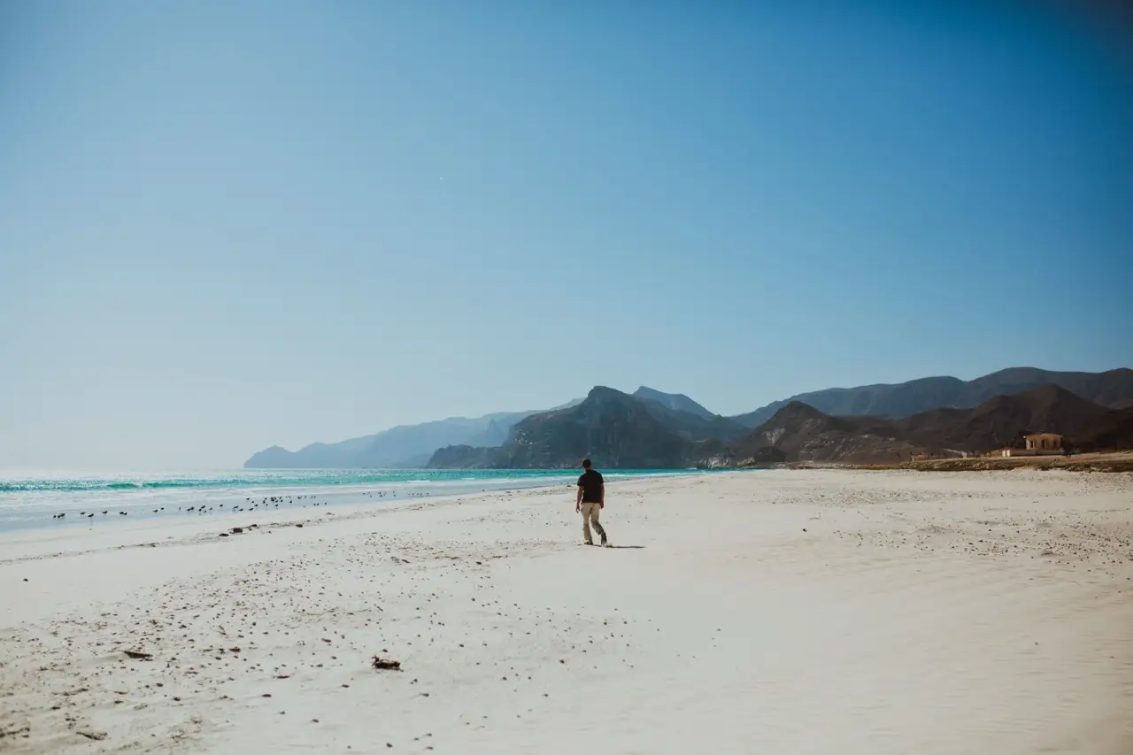 Een gast wandelt over een leeg strand met bergen aan de horizon.