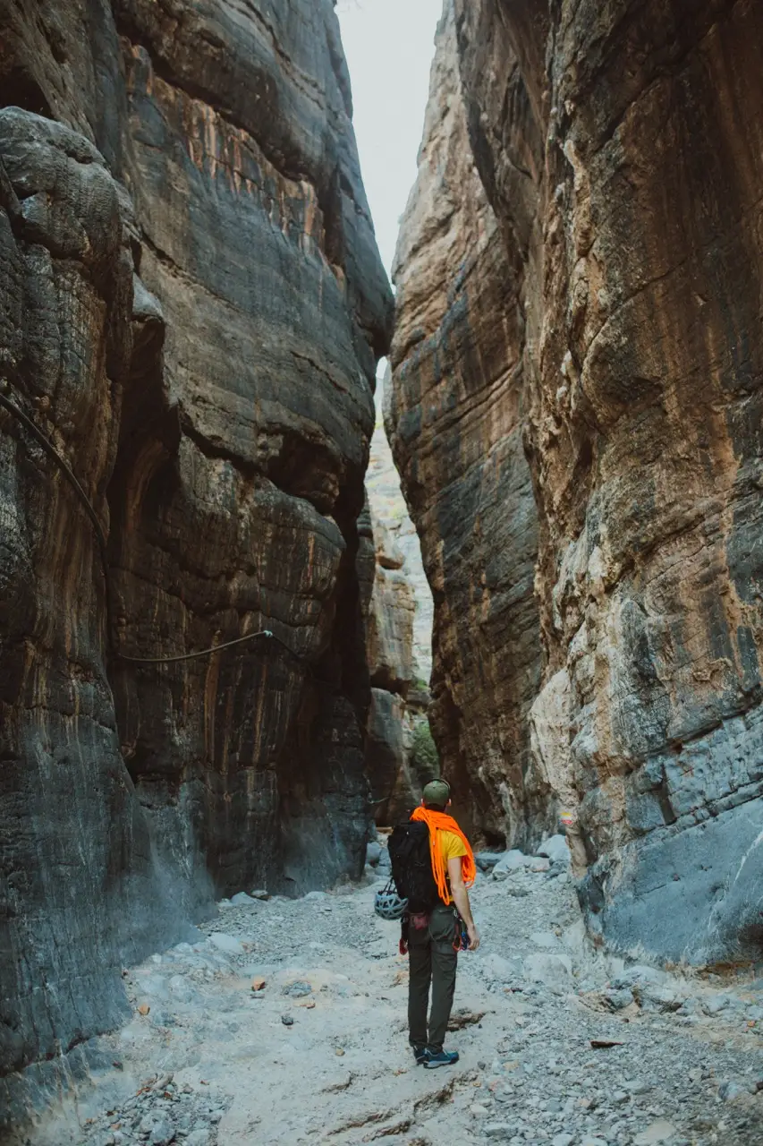 A hiker walking between the high walls of a narrow canyon.