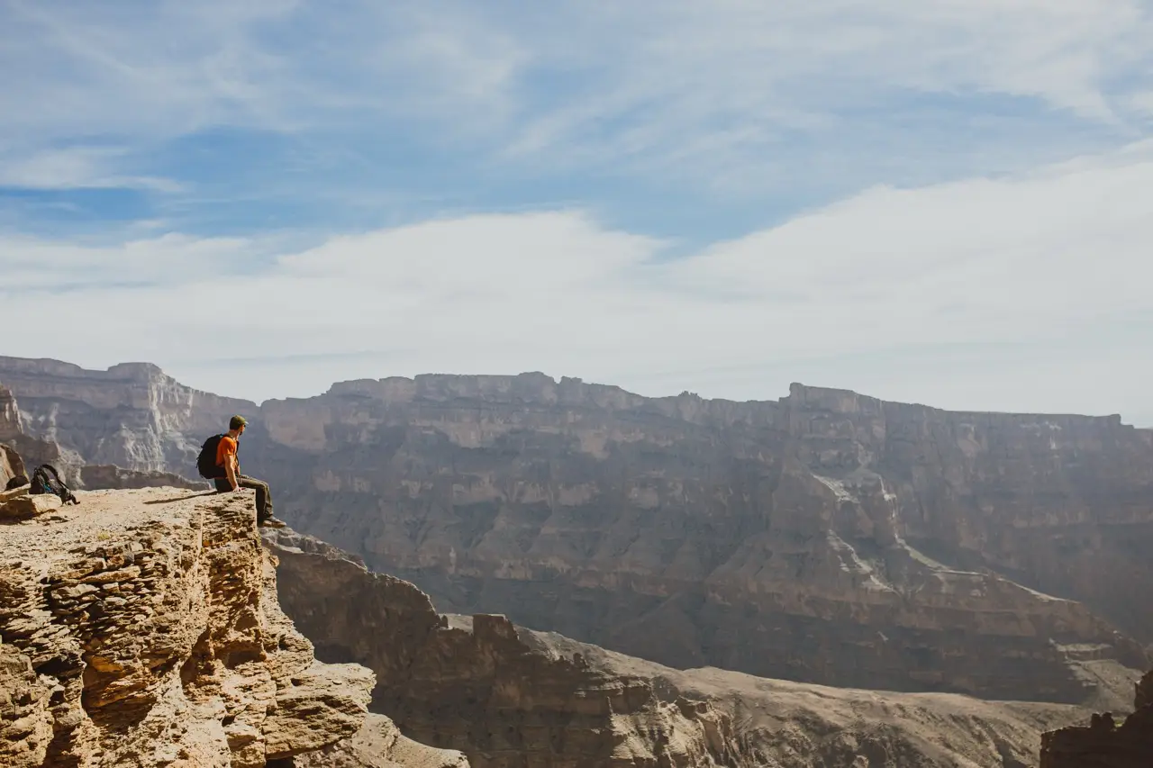 A guest sitting on a rock ledge above a wide canyon.
