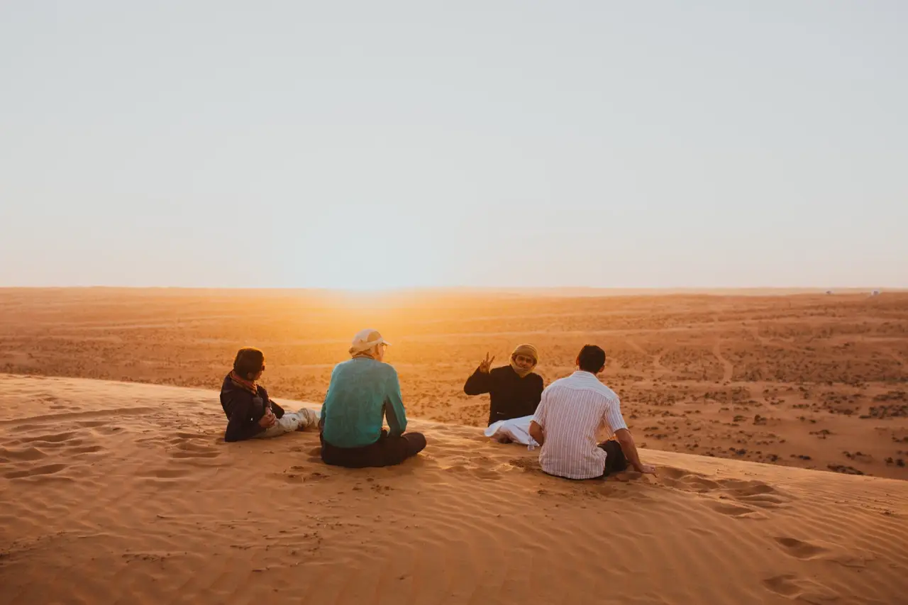 Four guests sitting on a dune, watching the sun set over the desert.