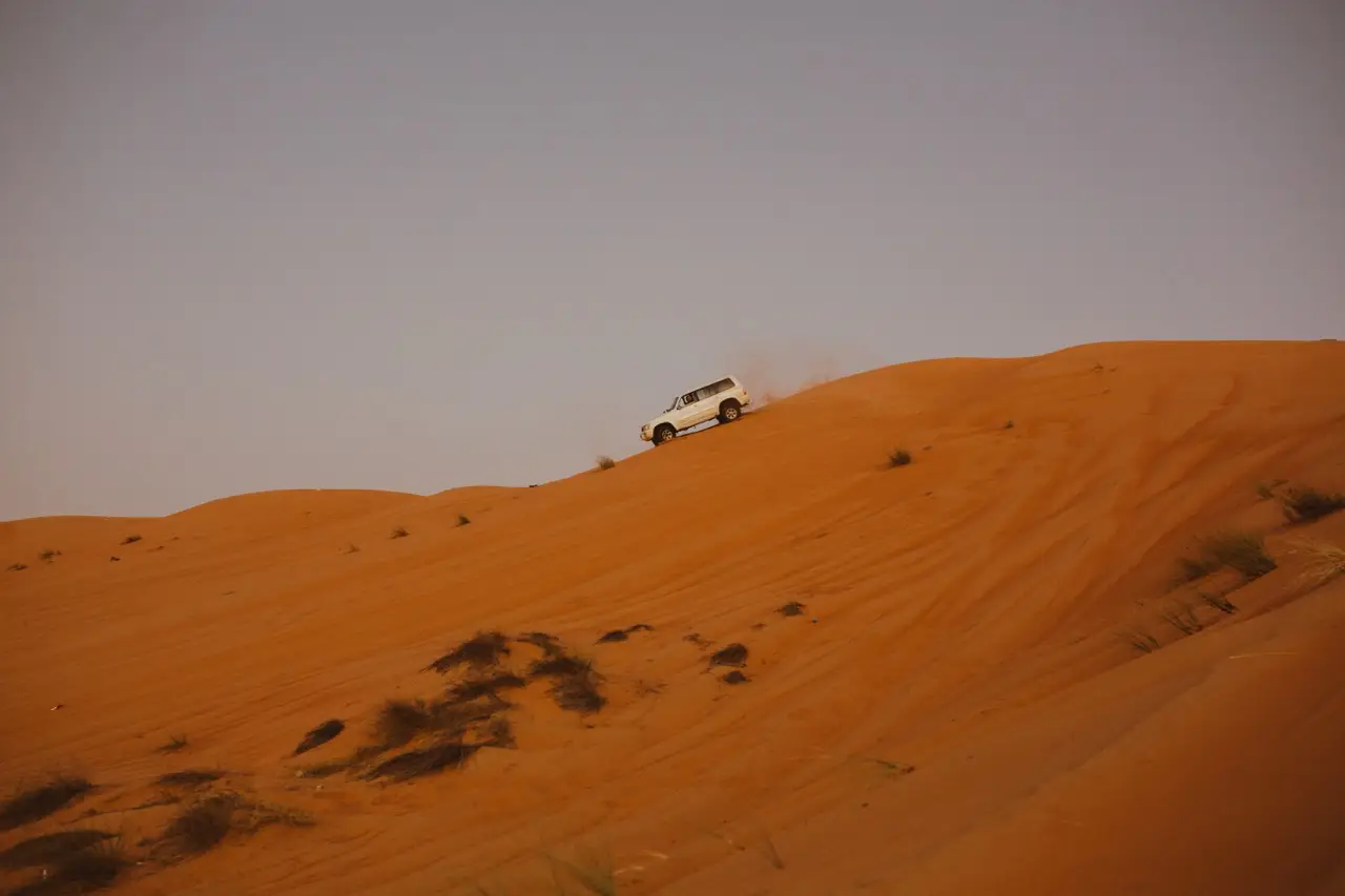 A 4×4 on the crest of a tall orange dune at dusk.