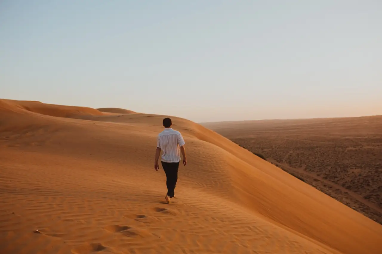 A guest walking along a sharp orange dune ridge at golden hour.