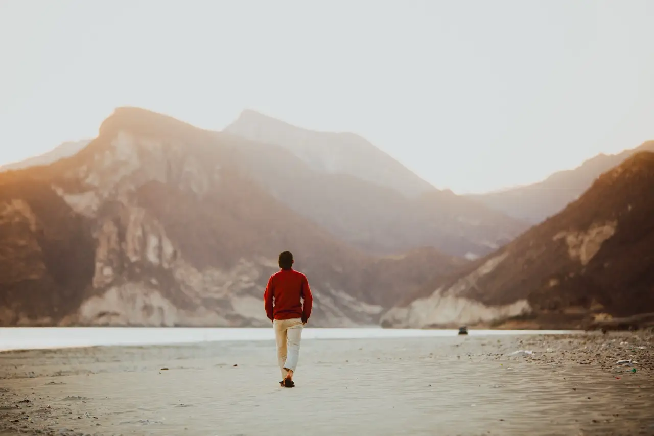 A guest walking along a lakeshore toward hazy mountains.