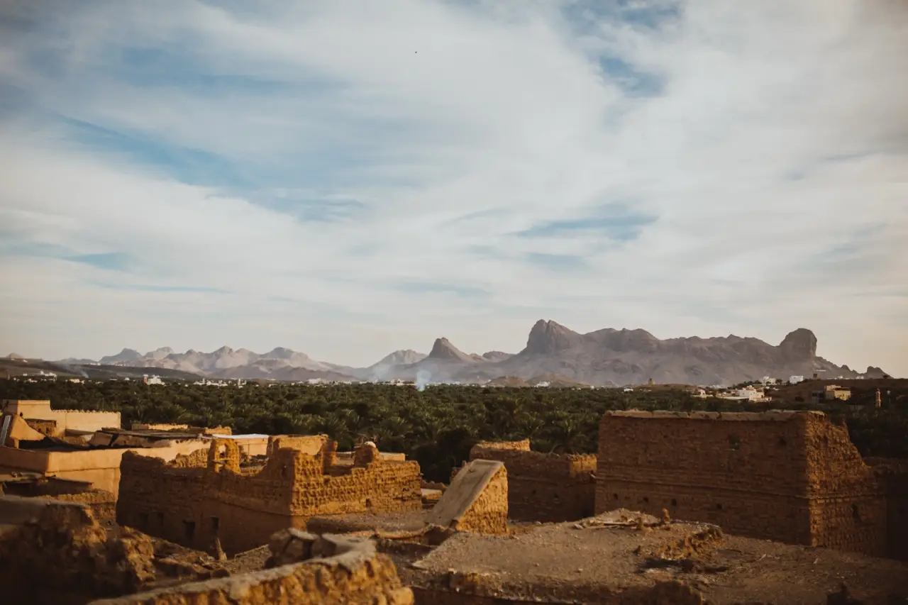 Ruined mud-brick houses in front of a jagged mountain ridge.