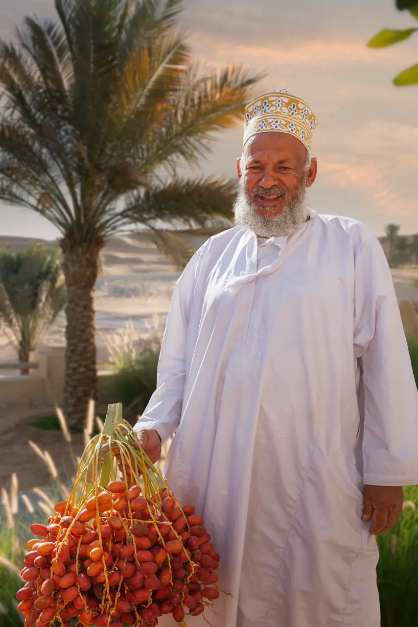 An Omani man in a kummah cap holding a branch of fresh dates.