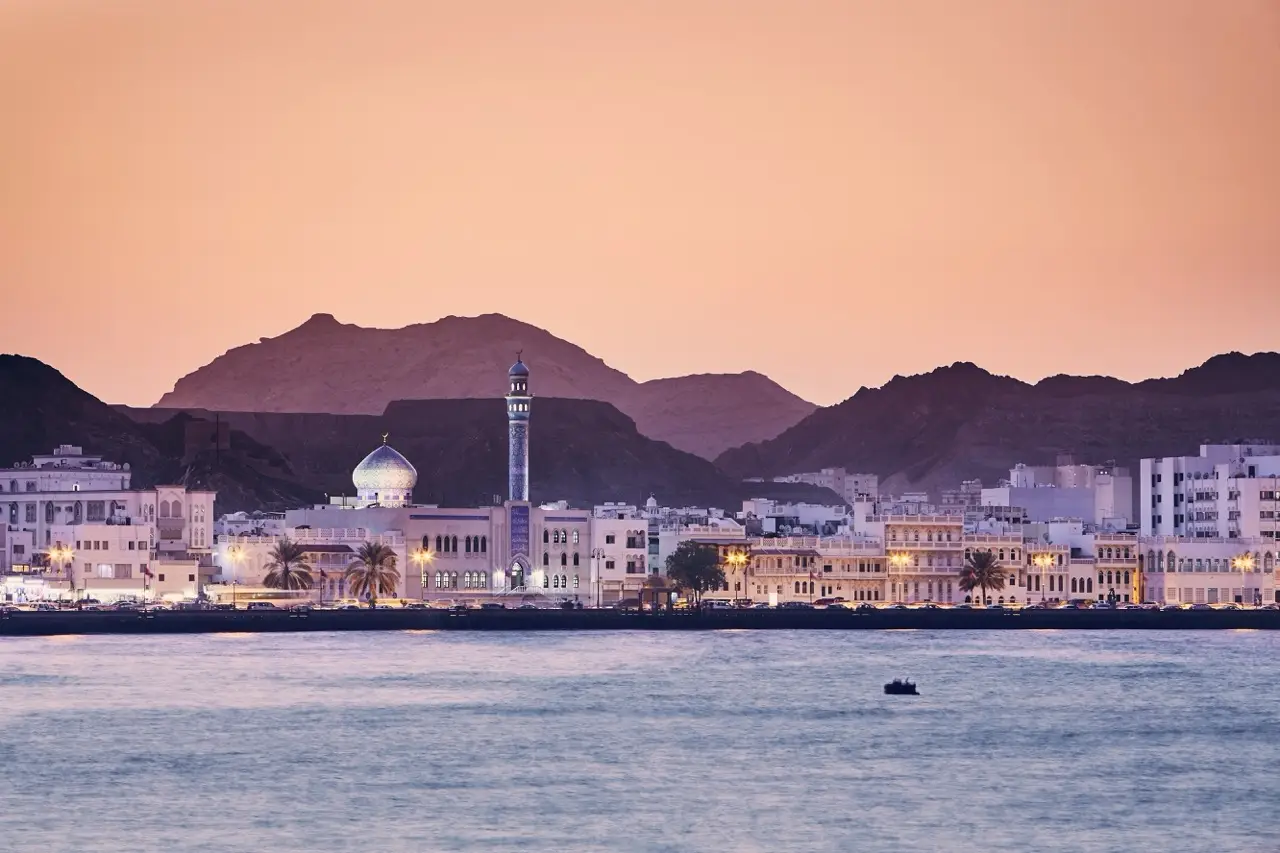Muscat’s waterfront and mountains at golden hour.