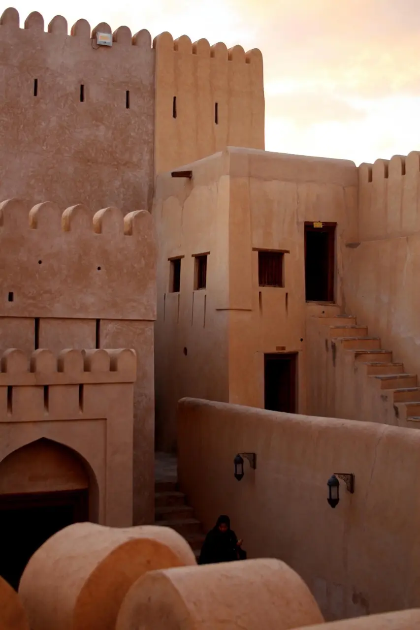 A woman walking down the stairs between the mud-brick walls of Nizwa Fort.